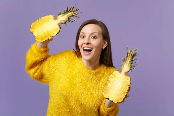 Giovane donna allegra in maglione di pelliccia che tiene in mano metà di frutta fresca matura all'ananas isolata su sfondo viola pastello. Persone vivido stile di vita, rilassarsi concetto di vacanza. Falsificare spazio di copia . — Foto Stock