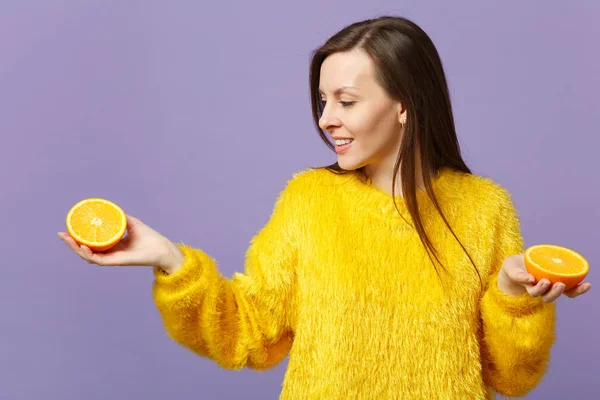 Mujer joven y bonita en suéter de piel que sostiene la mirada en mitades de fruta naranja madura fresca aislada sobre fondo pastel violeta en el estudio. La gente estilo de vida vívido relajar concepto de vacaciones. Simular espacio de copia . —  Fotos de Stock