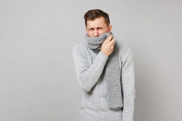 Chory młody człowiek w szarym swetrze pokrycie usta z szalik sneez — Zdjęcie stockowe