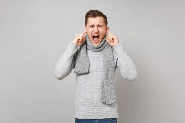 Ερεθισμένος νέος άντρας με γκρι πουλόβερ, κασκόλ ουρλιάζοντας, που καλύπτει e — Φωτογραφία Αρχείου
