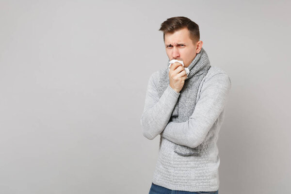 Young man in gray sweater, scarf coughing and covering mouth wit