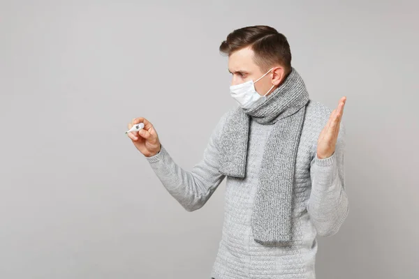 Young man in sweater, scarf sterile face mask looking on thermom