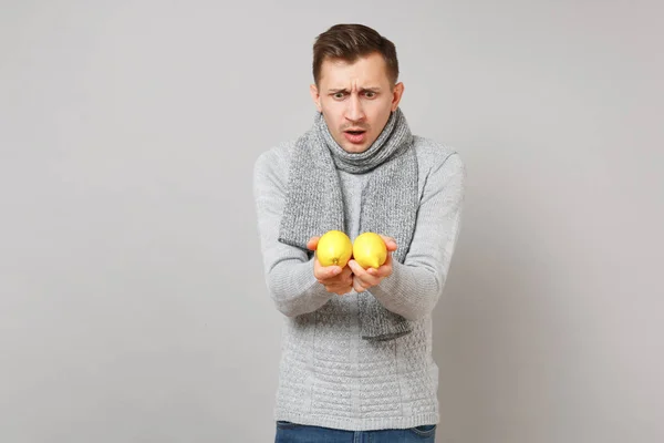 Joven sorprendido en suéter gris, bufanda mirando limones en ha — Foto de Stock