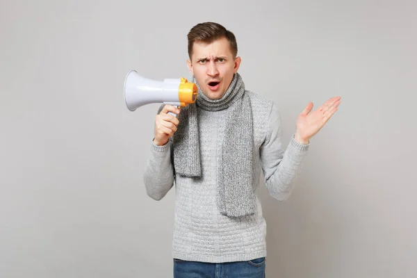 Förbryllad ung man i grå tröja, halsduk hålla MegaFon spridning — Stockfoto