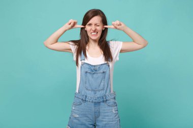 Mavi turkuaz arka plan stüdyo portresi üzerinde izole edilmiş günlük kot elbiseli esmer kadın. İnsanların yaşam tarzı konsepti. Kopyalama alanı oluşturun. Parmaklarıyla kulaklarını kapatıyor.