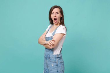 Mavi turkuaz arka planda izole edilmiş günlük kot elbiseli esmer bir kadının yan görünüşü. İnsanların yaşam tarzı konsepti. El ele tutuşmak, kameraya bakmak, ağzını açık tutmak.