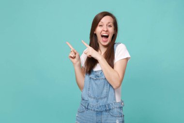 Mavi turkuaz arka planda izole edilmiş sıradan kot elbiseli esmer kadın. İnsanların yaşam tarzı konsepti. Kopyalama alanı oluşturun. İşaret parmaklarını bir yana koyup, ağzını açık tutmak.
