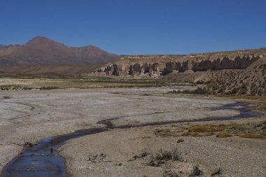 Eroded cliffs along the wide valley of a tributary of the River Lauca high on the Altiplano of northern Chile in Lauca National Park. clipart