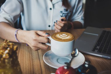 Ahşap masa üzerinde latte taşıyan kadın elleri