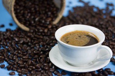 Bir fincan kahve ve bir çuval kavrulmuş kahve. mavi sırtüstü