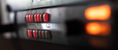 TV stüdyosu yakın çekim içinde ön planda bulanık turuncu ışıklar ile siyah bir cihazda kırmızı düğmeler.