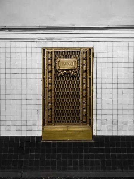 セラミックタイルと黒と白の壁の背景に古い装飾真鍮金属ドア 地下鉄駅の線路の壁に飾られた金属製の扉 — ストック写真