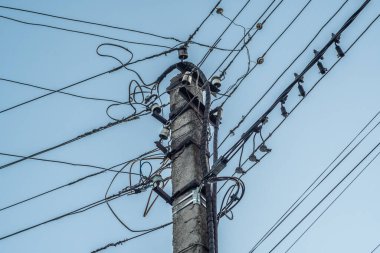 Eski beton elektrik desteği kaotik bir şekilde birçok kabloyla asılmış, yakın plan..