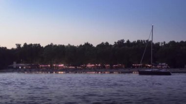 Yat, akşamları açık hava plaj kulübünün arka planında yüzer..