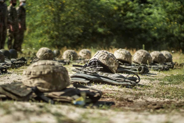 Military helmets and bulletproof vests are lined up on the grass.