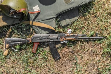 Kyiv, Ukrayna - Temmuz 2020: Kullanılan AK-74 makineli tüfek kurşun geçirmez yelek ve kaskın yanındaki çimlerin üzerinde yatıyor.