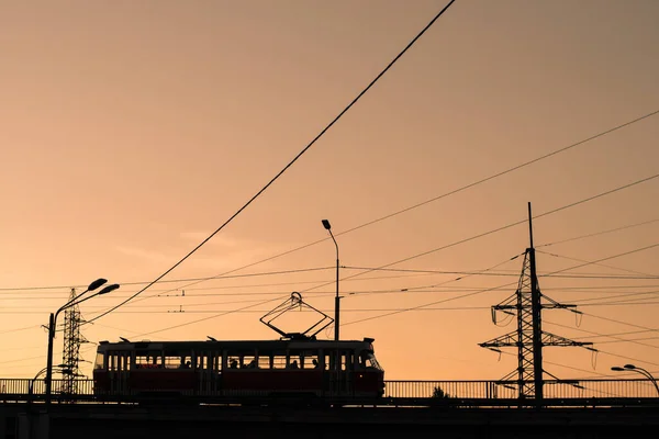 Silhouette of a tram at sunset at dusk on the background of power lines and towers.