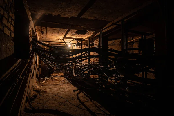 An old underground brickwork cable tunnel or basement with cables with tungsten lamp lighting.