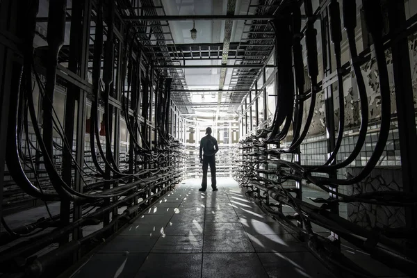 Silhouette of a man with a lantern in a dark cable tunnel with many cables. Cable cabinet of automatic telephone exchange.