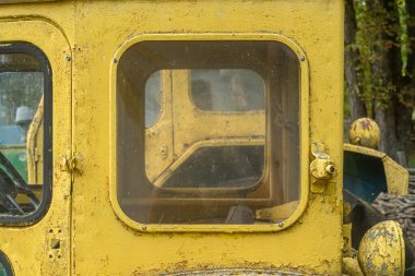 Eski sarı traktör kabininin yan penceresinde yıpranmış boya ve tozlu camlar. Pereiaslav, Kyiv Oblastı, Ukrayna, 13 Eylül 2025.