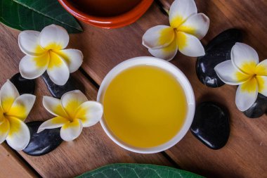 Plumeria çiçek ve ahşap yüzey üzerinde siyah yuvarlak taşlar ile masaj yağı