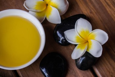 Plumeria çiçek ve ahşap yüzey üzerinde siyah yuvarlak taşlar ile masaj yağı