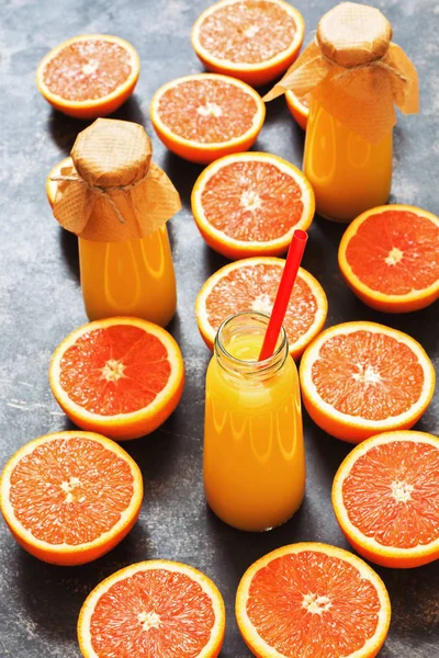 Orange juice in a bottle and halves of orange on a dark background