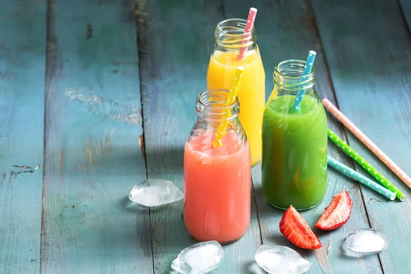 Colorful drinks in bottles . Pink, yellow and green drink on a blue wooden table. Copy space.