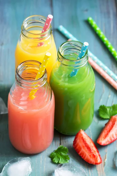 Colorful drinks in bottles . Pink, yellow and green drink on a blue wooden table.