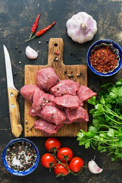 Raw beef meat cut into pieces, spices, cherry tomatoes, garlic and parsley. The view from above, flat lay