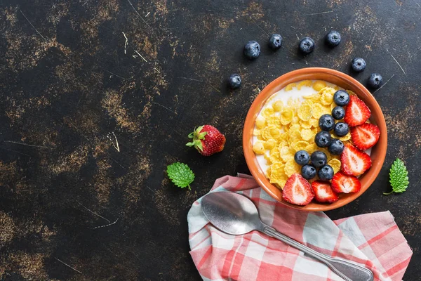 Corn flakes with milk, strawberries and blueberries on a dark background. View from above, flat lay