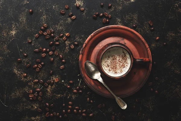 Coffee in a vintage brown ceramic cup on a dark grunge background with roasted coffee beans. Top view, copy space.