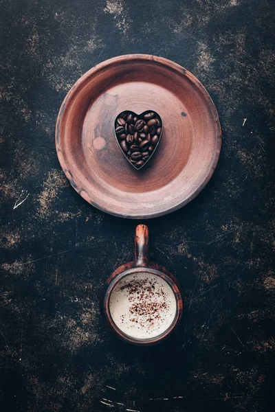 Heart of coffee beans and hot coffee drink in a vintage cup on a rustic dark background. Valentine\'s Day.Top view, place for text