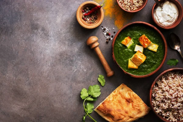 Palak paneer or Spinach and Cottage cheese curry,mortar with spices , naan, rice on a dark background. Traditional Indian food. Overhead view, copy space.