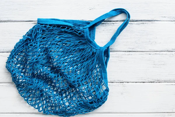 Blue cotton mesh bag on a white rustic wooden board background. Top view, flat lay, copy space.