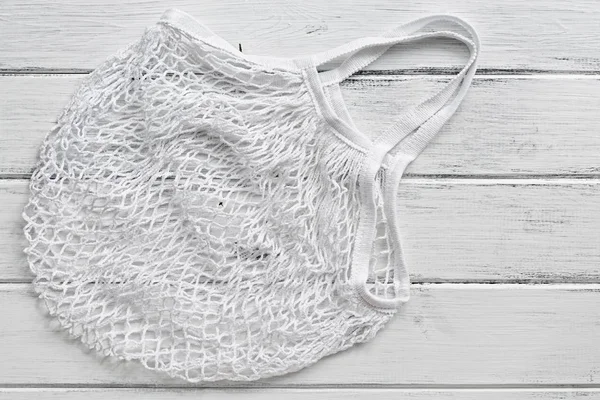 White cotton mesh bag on a white rustic wooden board background. Top view, flat lay, copy space.