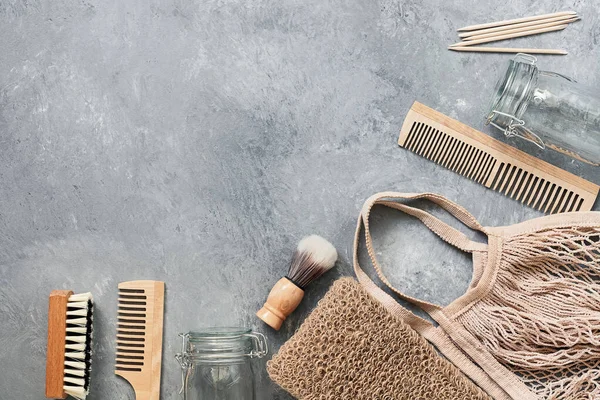 Zero waste. Bath and home accessories. Cotton bag, glass jar, wooden comb, wooden shaving brush, cuticle pusher, brush, loofah washcloth on a gray background. Flat lay, top view.