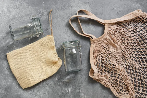 Cotton mesh bag and glass jars on a dark background, top view, flat lay. Zero waste.