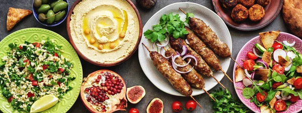 Assorted Middle Eastern and arabic dishes on a dark rustic background,border. Hummus,tabbouleh, salad Fattoush,pita,meat kebab,falafel,baklava,pomegranate. Halal food.Top view, flat lay, copy space