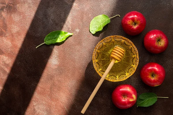 Red apples and honey on a dark background with shadows and sunlight. Top view, flat lay, copy space