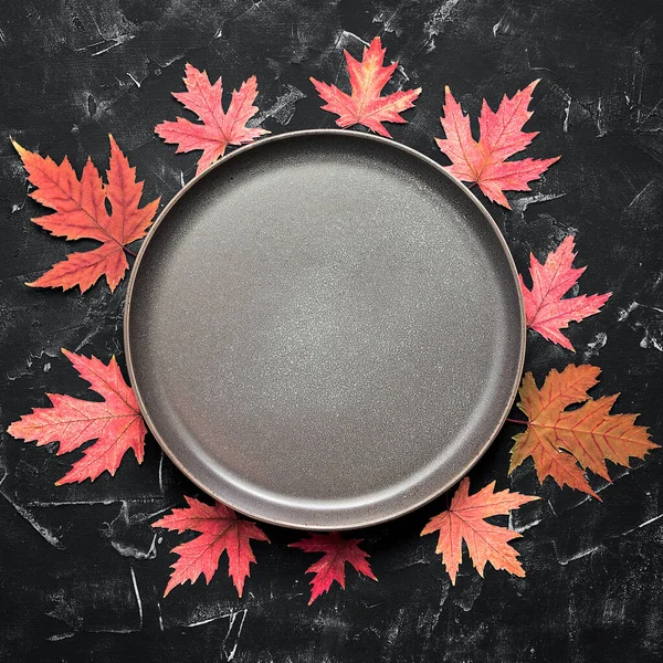 Autumn modern minimal kitchen still life. Empty plate and frame made of red dry maple leaves. Top view, flat lay, copy space