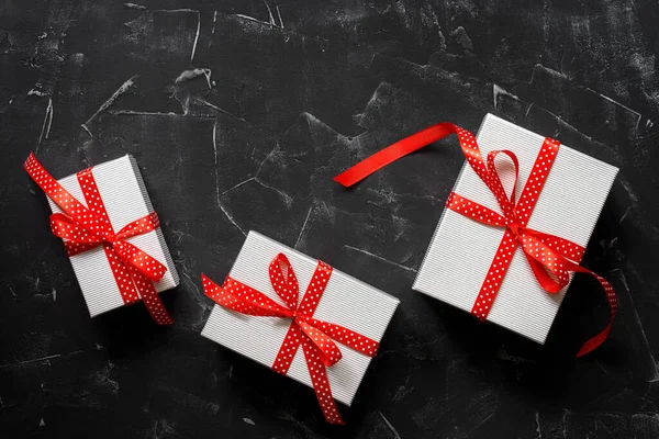 Three gift boxes with a red ribbon on a black stone background. Present and holiday concept. Top view, flat lay.