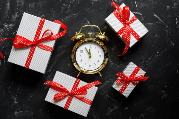 Alarm clock and gift boxes with red ribbon on black stone background. Modern creative still life. Top view, flat lay.