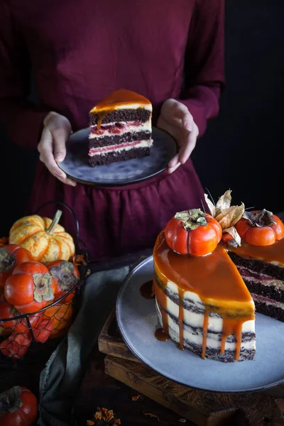 Autumn cake with persimmon and caramel with a pumpkin and a girl in a burgundy dress on a black background, Atmospheric dark food photos, Pastry Homemade in Womans hands, Selective focus — Stock Photo, Image