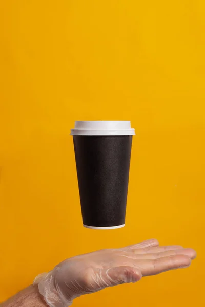 A hand in a glove holds a disposable cup