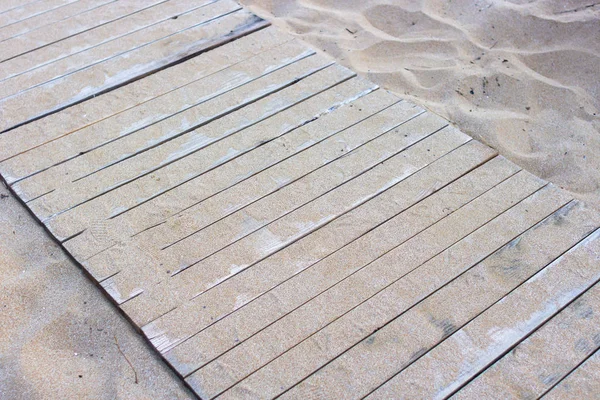 Wooden background. Boards in the sand. Wooden walkway on the sandy beach. Natural materials. The texture of the wooden surface. Beach landscape.