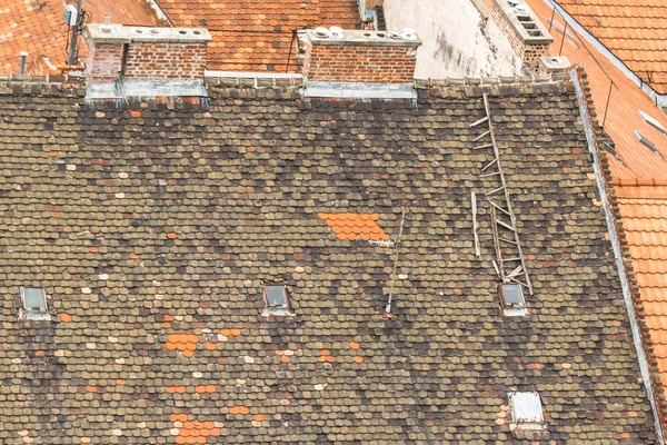 View of the old roofs. City on top. Exterior in grunge style. A collapsing house. European roofs. The architecture of old Budapest. City landscape from a height. Broken stairs on a tiled roof.