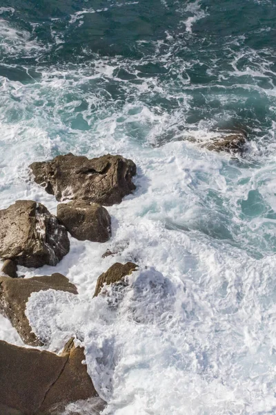 Bay of Biscay. Raging force of nature. Waves lick stones and beat against rocks. Spanish coast. Salty sea air. Boulders and stones in the spray of sea waves. Seascape view from above. Sound of waves. Foam of waves on a stone block.