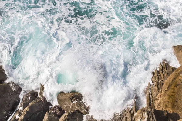 Bay of Biscay. Raging force of nature. Waves lick stones and beat against rocks. Spanish coast. Salty sea air. Boulders and stones in the spray of sea waves. Seascape view from above. Sound of waves. Foam of waves on a stone block.