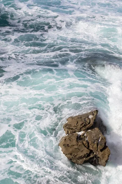 Bay of Biscay. Raging force of nature. Waves lick stones and beat against rocks. Spanish coast. Salty sea air. Boulders and stones in the spray of sea waves. Seascape view from above. Sound of waves. Foam of waves on a stone block.